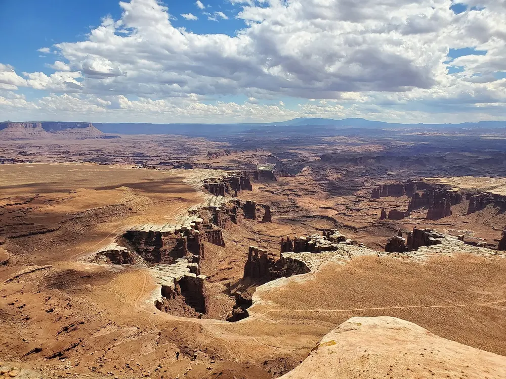 View from White Rim Overlook in Canyonlands National Park of branching canyons with a pale rock band and distant mesas under clouds