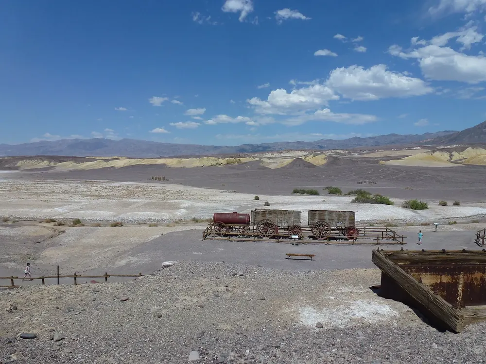 Harmony Borax Works in Death Valley National Park: remains of the borax plant with historic wagons on a barren plain, hills and mountains behind