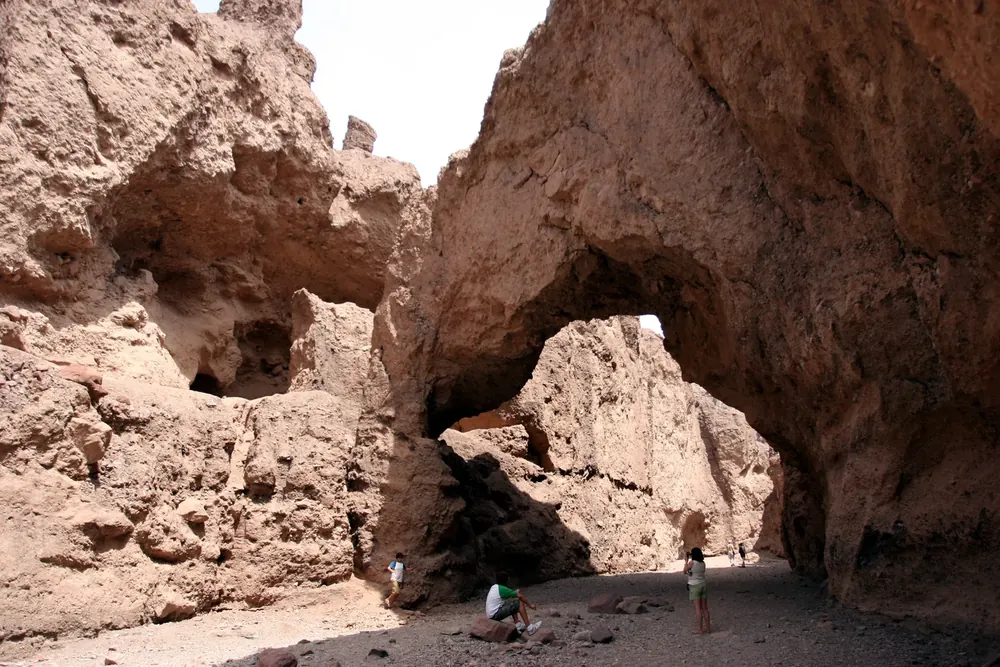 Natural Bridge in Death Valley National Park: a massive rock bridge spanning a canyon of light brown rock, with small hikers beneath