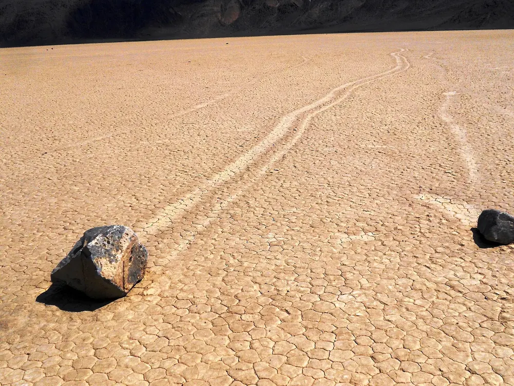 Racetrack Playa in Death Valley National Park: dark moving rocks with long trails across the cracked, dried-out lake bed