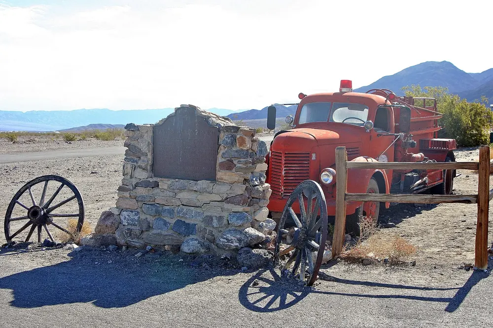 Stovepipe Wells in Death Valley National Park: historic memorial stone, an old red fire engine and wagon wheels in front of desert mountains