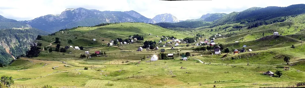 Panorama of the village of Nedajno on the green plateau, meadows all around, the mountains of Durmitor behind