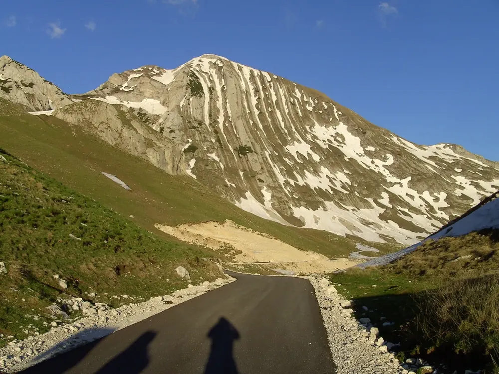 The summit of Prutaš in Durmitor National Park with strikingly folded rock layers and patches of snow, a mountain road in the high valley in front