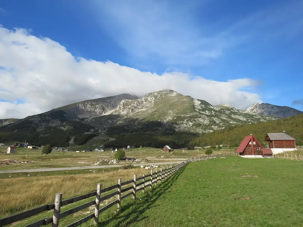 Savin Kuk in Durmitor National Park above the hamlet of Motički Gaj: green alpine meadows, a wooden fence and a red hut in front of the massif