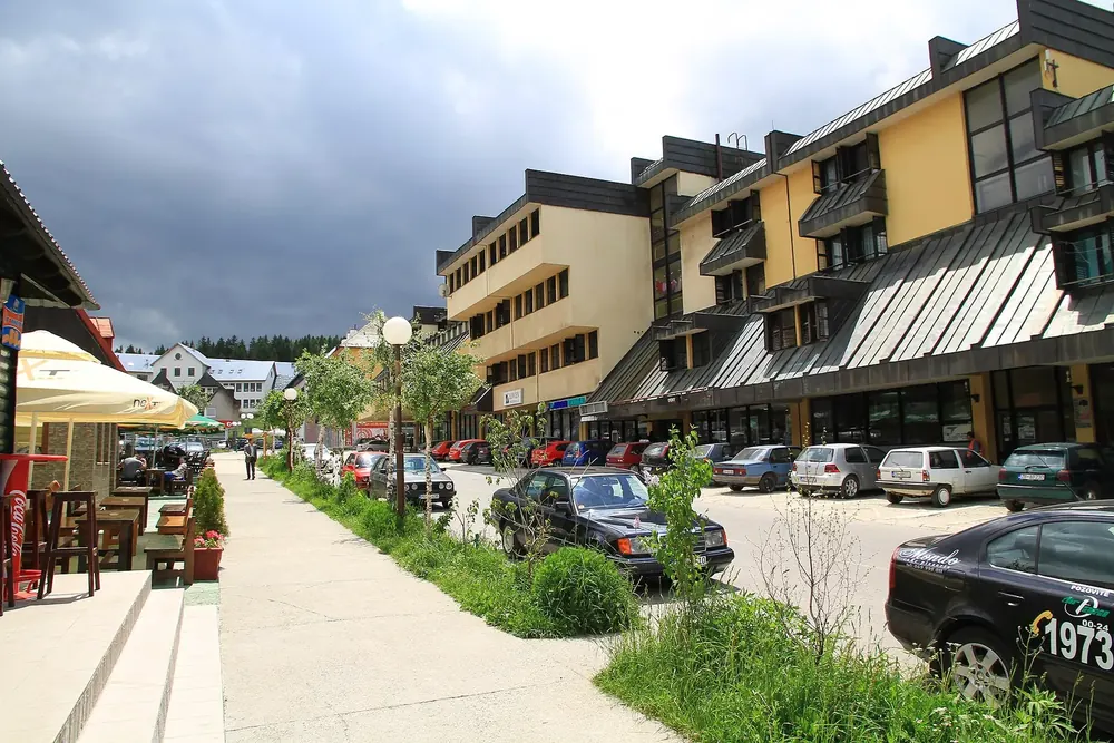 Main street of Žabljak: a row of shops with cafés and parking spaces under a cloudy sky