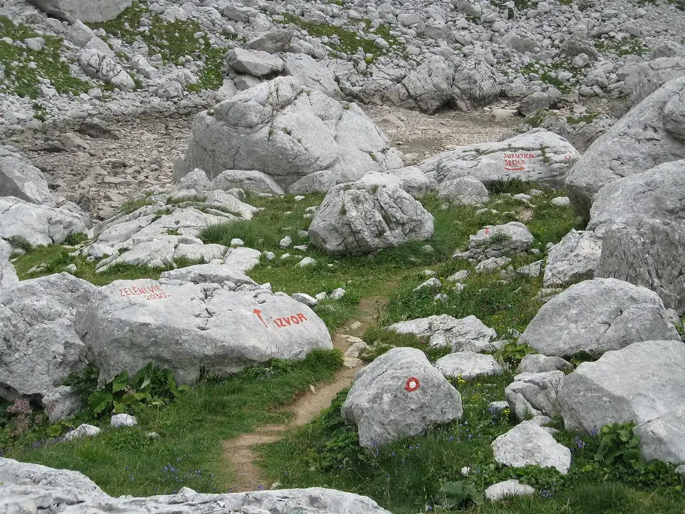 The dried-out basin of Zeleni Vir in Durmitor National Park: pale limestone blocks and patches of grass, red trail markings on the stones