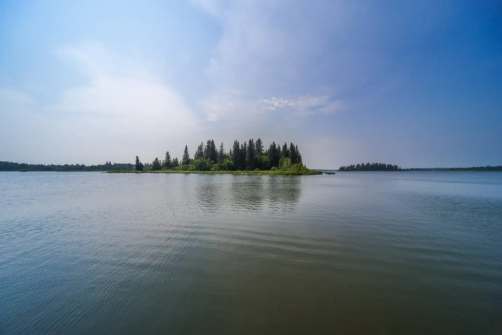 Astotin Lake in Elk Island National Park near the campground: a still lake with a forested island under a pale sky