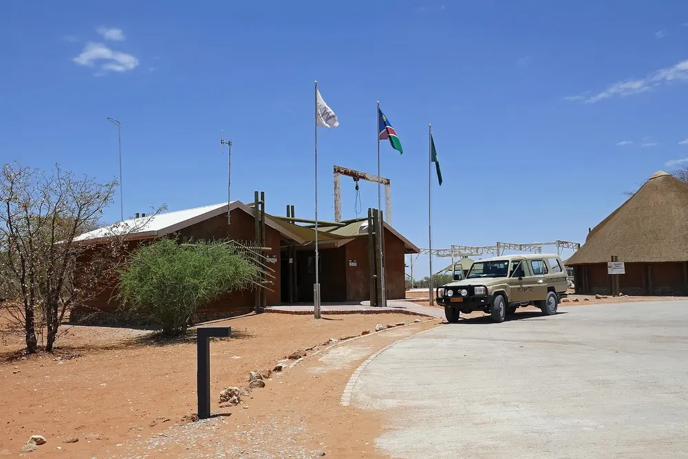 Olifantsrus Camp in Etosha National Park: reception building with flags, thatched hut and 4x4 under a blue sky.