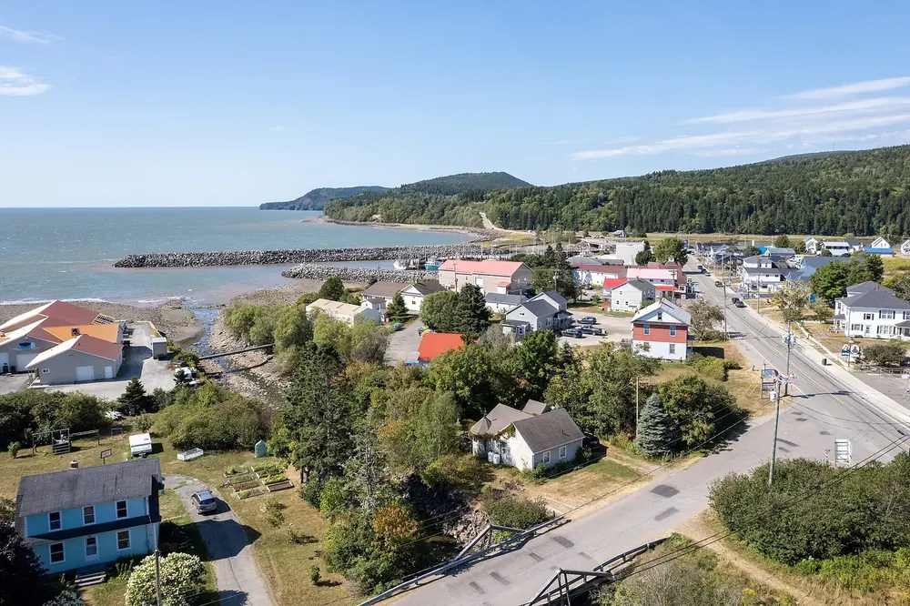Aerial view of Alma on the Bay of Fundy: houses along the main street, harbour breakwater and forested coast