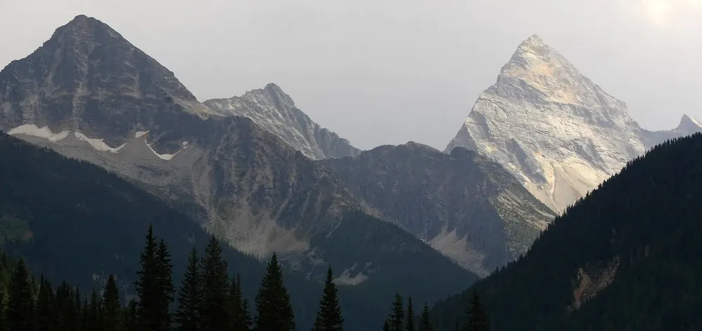 Mountains in Glacier National Park in Canada near Rogers Pass, the pointed Mount Sir Donald on the right above dark conifer forest