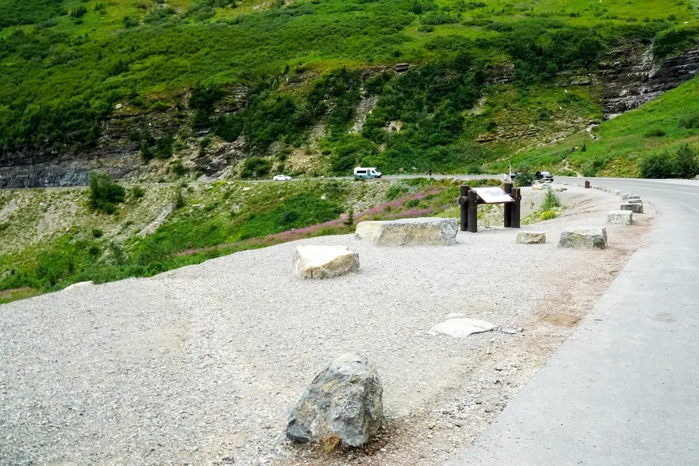 Big Bend on the Going-to-the-Sun Road in Glacier National Park, Montana: a pull-out with stone blocks and information boards below green mountain slopes