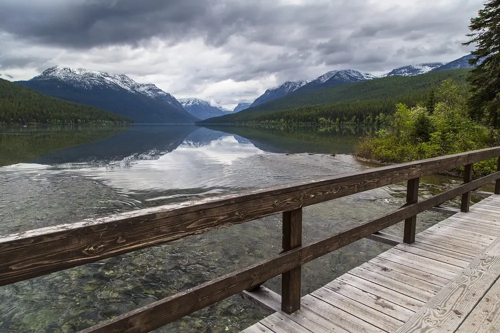 Wooden footbridge at the foot of Bowman Lake in Glacier National Park, Montana, with the long lake between wooded mountains and reflections behind