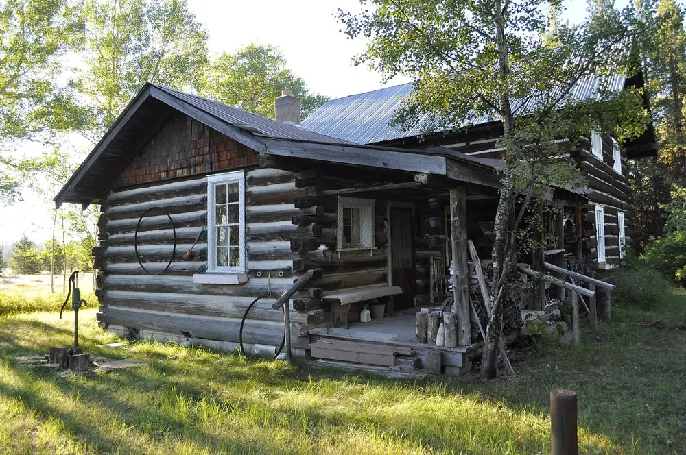 Vance Lodge in Polebridge: a historic log cabin with a porch and tin roof in a meadow among deciduous trees