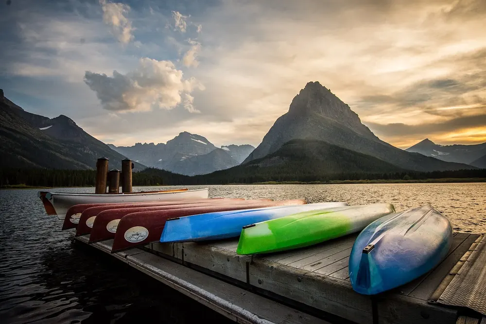 Kayaks and canoes on a dock at Swiftcurrent Lake in Glacier National Park, Montana, with the pointed Grinnell Point in evening light behind