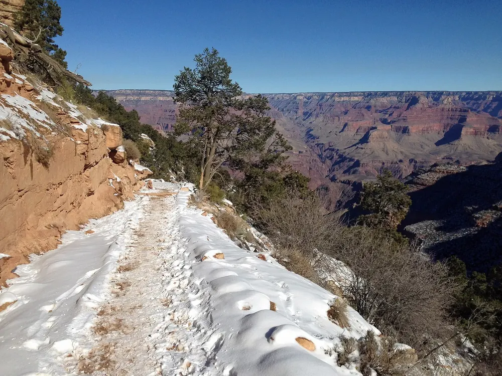 Snow-covered upper section of the Bright Angel Trail at the rim of Grand Canyon National Park, the vast canyon behind