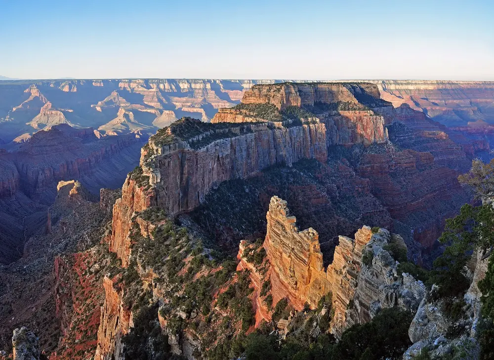 Sunrise at Cape Royal in Grand Canyon National Park: reddish glowing rock towers and mesas above the wide canyon