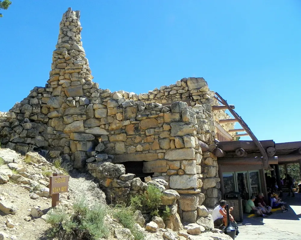 Hermits Rest in Grand Canyon National Park: a rustic rest house of natural stone walls with a tall chimney on the canyon rim, rocks and shrubs in front