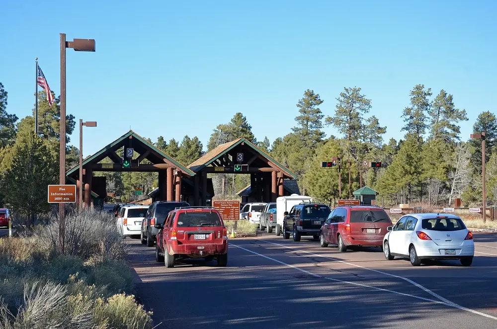 The South Entrance Station of Grand Canyon National Park: fee booths under wooden roofs, waiting cars among pines in front