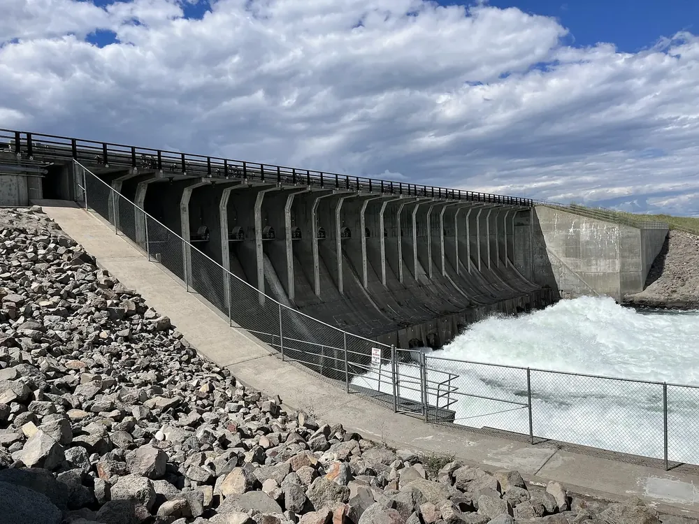 Jackson Lake Dam in Grand Teton National Park, seen from the side: a concrete dam wall with piers, foaming water and rock fill below