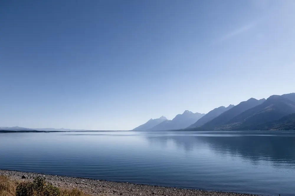 Calm Jackson Lake in Grand Teton National Park in blue evening light, pebbles on the shore and the Teton Range behind