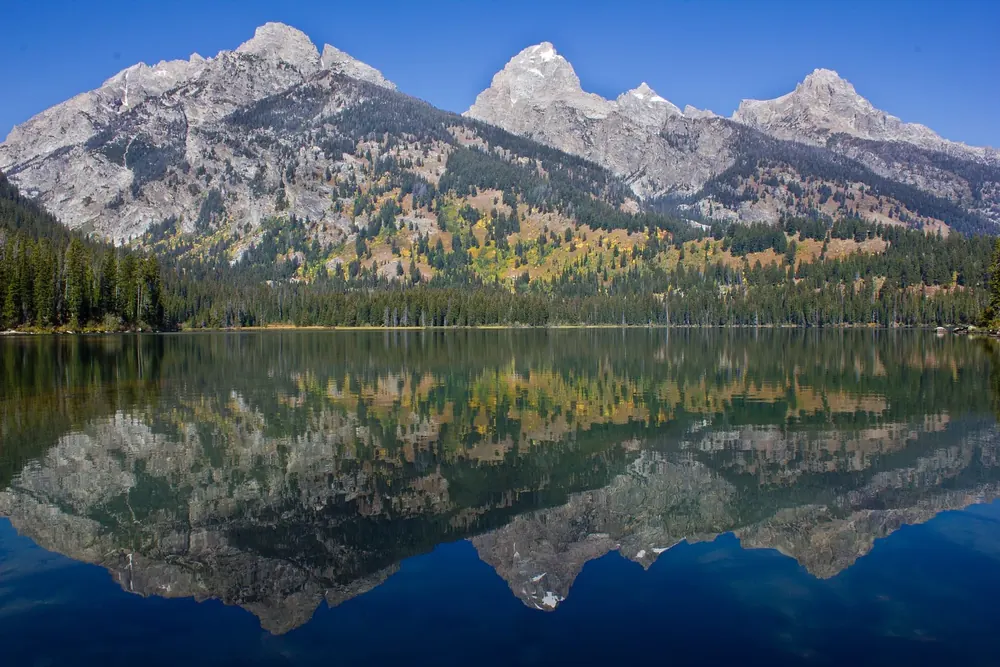 Taggart Lake in Grand Teton National Park: the peaks of the Teton Range and autumn forest reflected in the deep blue, still mountain lake