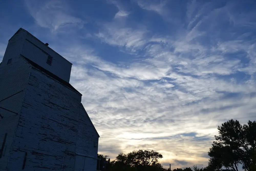 The old grain elevator of Val Marie as a dark silhouette against a dramatic evening sky with wispy clouds
