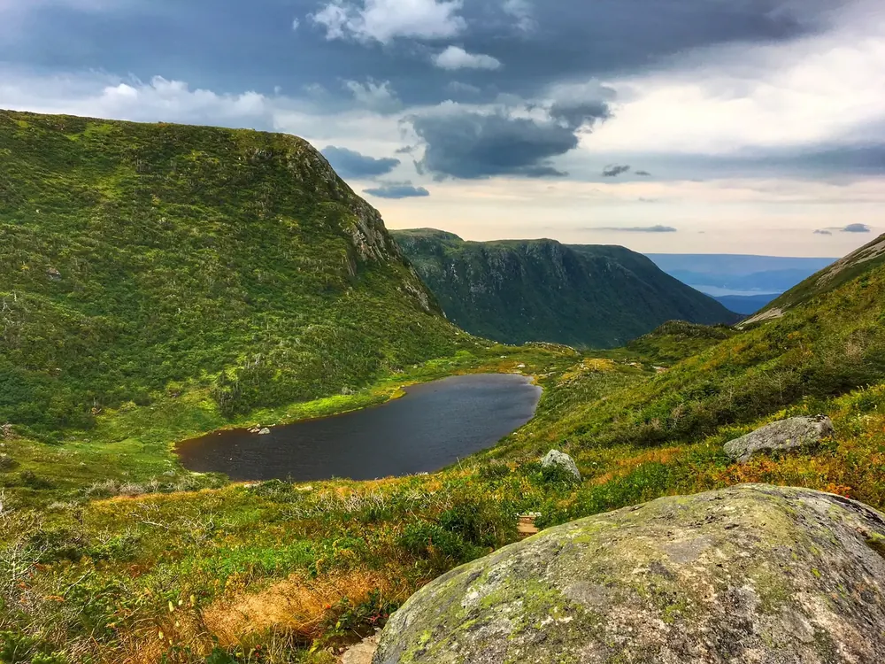 On the way up Gros Morne in Gros Morne National Park: green upland valley with a small lake between steep slopes, the fjord behind