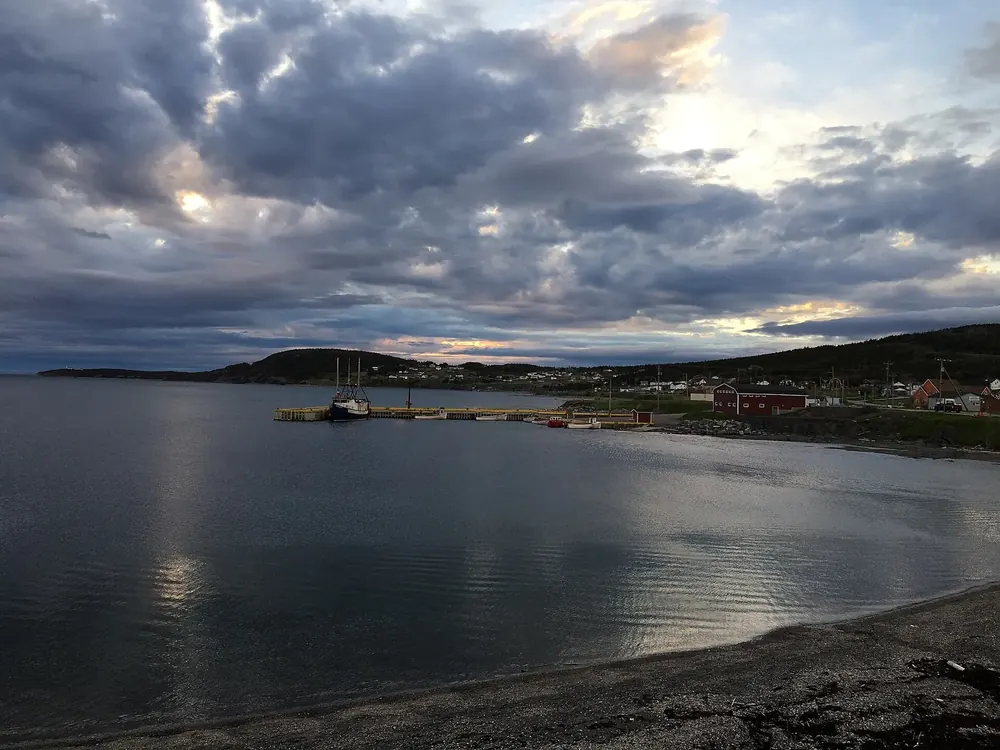 Dawn over the bay at Rocky Harbour, houses and a wharf on the shore under clouds