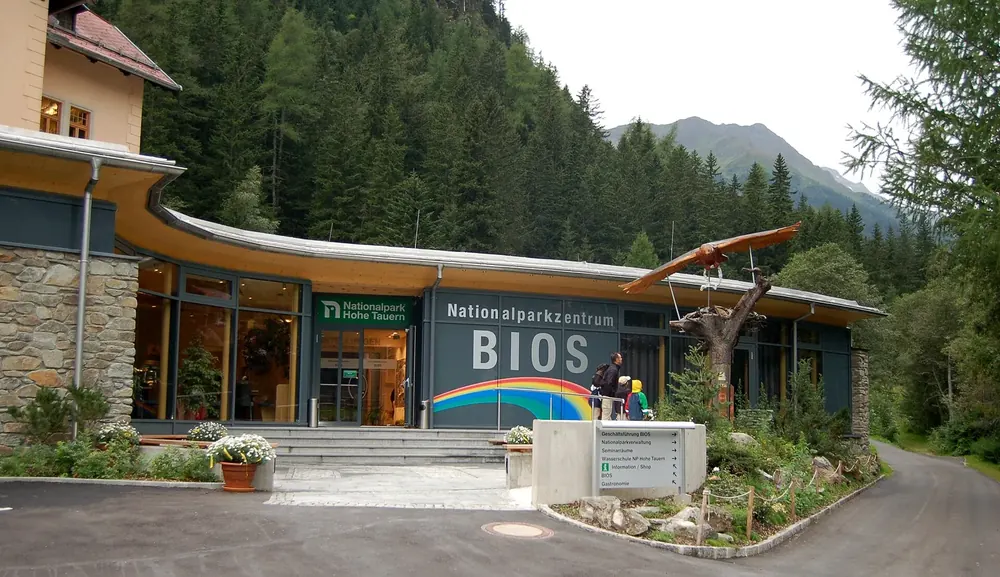 BIOS National Park Centre in Mallnitz: entrance building with a curved roof and lettering, mountain forest behind