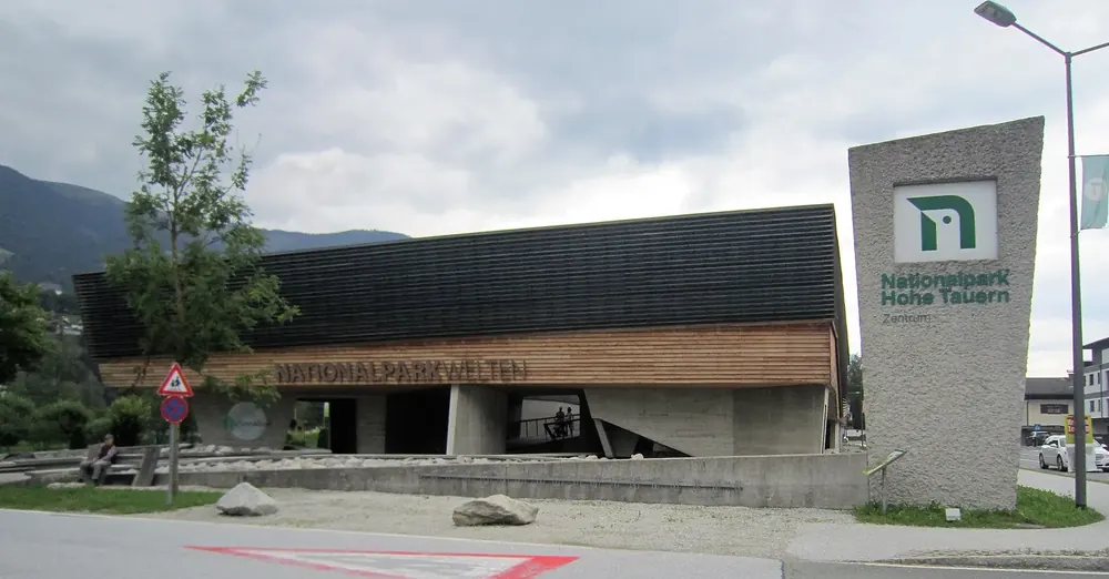 Nationalparkwelten in Mittersill: a low visitor centre with a timber facade, a pylon with the national park logo in front