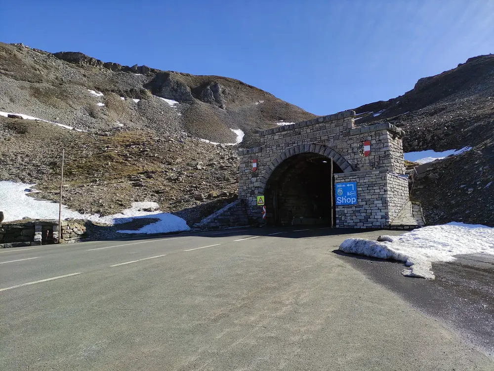 North portal of the Hochtor tunnel on the Grossglockner High Alpine Road near Hohe Tauern National Park: a masonry tunnel arch between patches of snow and scree