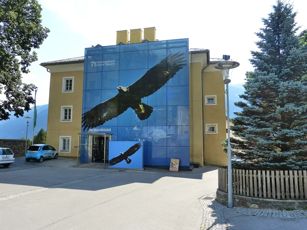 Matrei National Park House in East Tyrol: a historic school building with a blue glass facade printed with a golden eagle