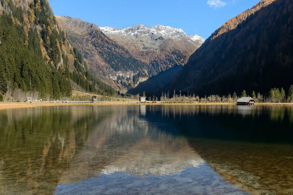 Stappitzer See in autumn: a clear lake with reflections, the Seebach Valley with snow-capped peaks behind