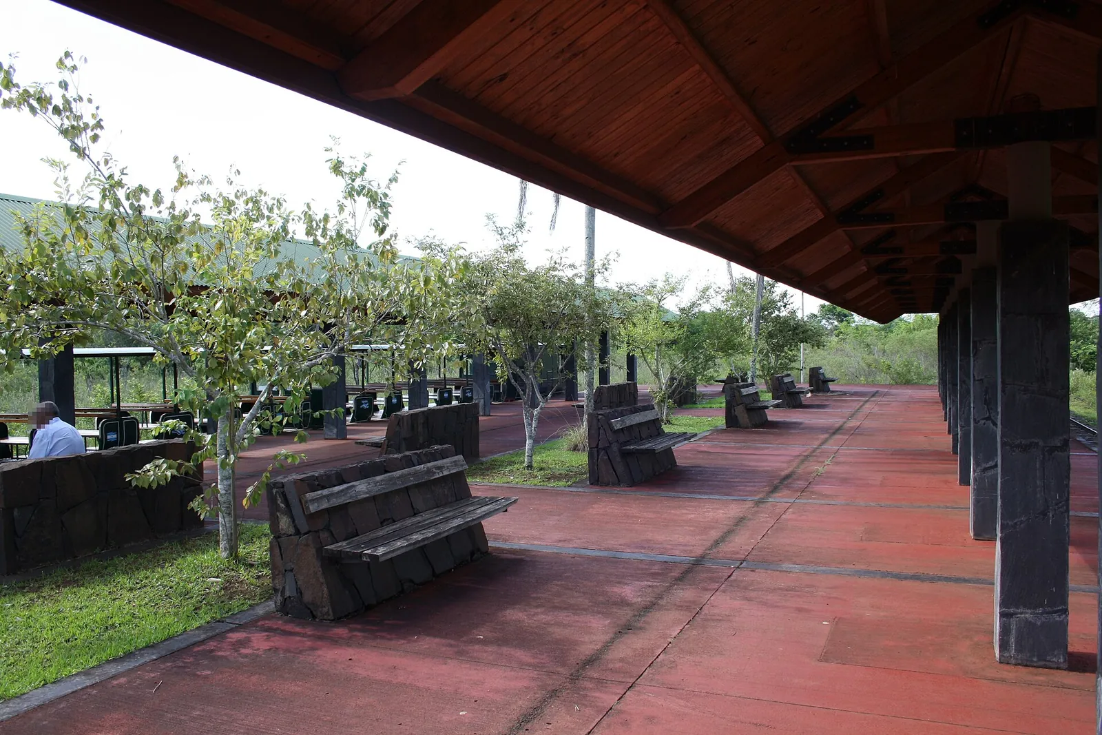 Covered platform of Estación Central in Iguazú National Park with red paving, wooden benches and a timber roof, trees and lawn alongside
