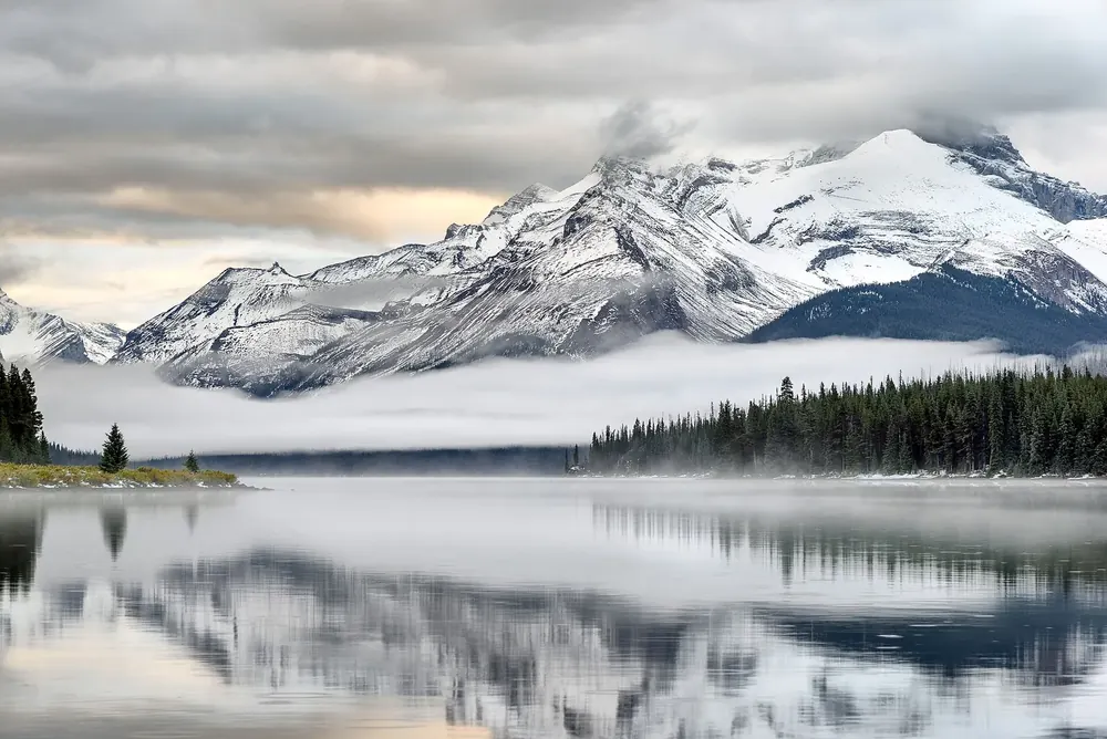 Sunrise at Maligne Lake in Jasper National Park: wisps of mist over the still lake below snowy mountains and conifer forest