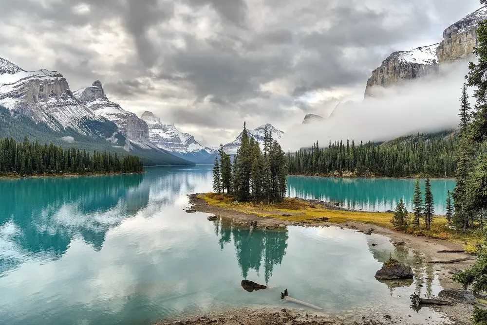 Spirit Island in Maligne Lake in Jasper National Park in the morning: small island with spruces in turquoise water below clouds and peaks
