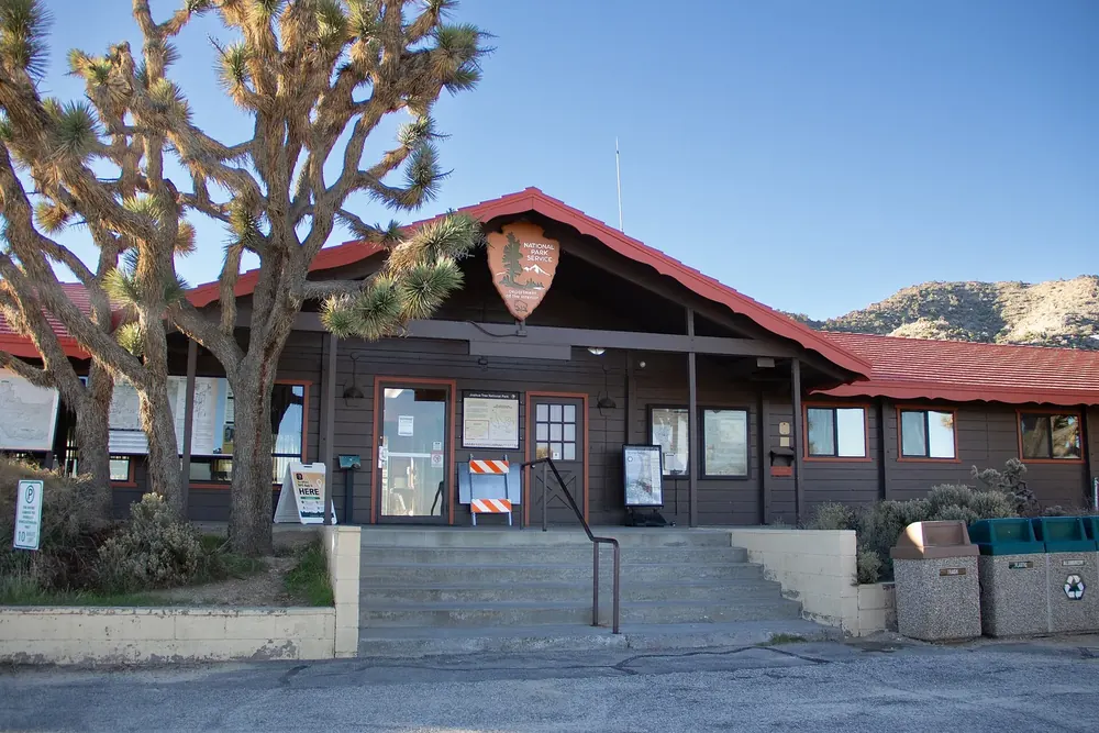 Black Rock Nature Center: a brown wooden building with a red roof and the park emblem, steps and Joshua trees in front