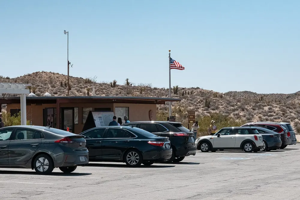Cottonwood Visitor Center: low light-brown buildings with a flagpole in front of desert hills, a full car park in front