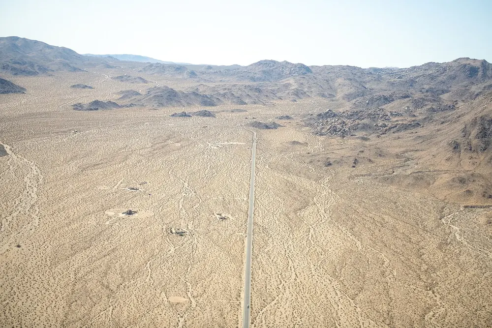 Aerial view of the north entrance: a straight road across the wide desert plain, lined by barren rocky mountains