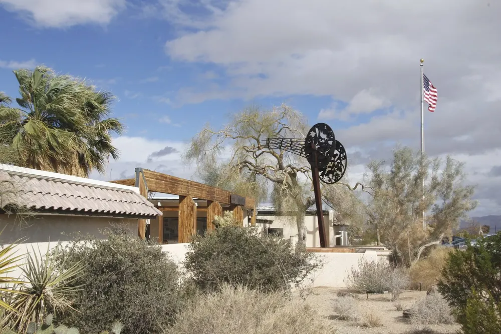 Oasis Visitor Center in Twentynine Palms: low buildings with a flagpole among fan palms and desert plants