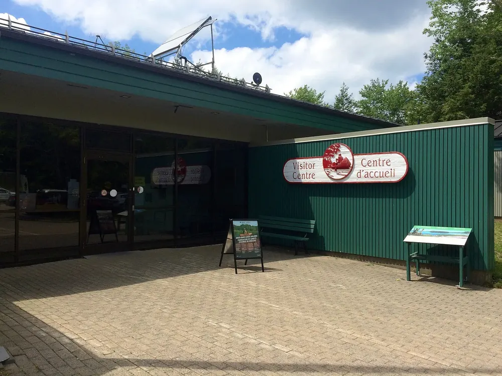 Kejimkujik National Park visitor centre: a low green building with a canopy and a bilingual sign, a paved square in front
