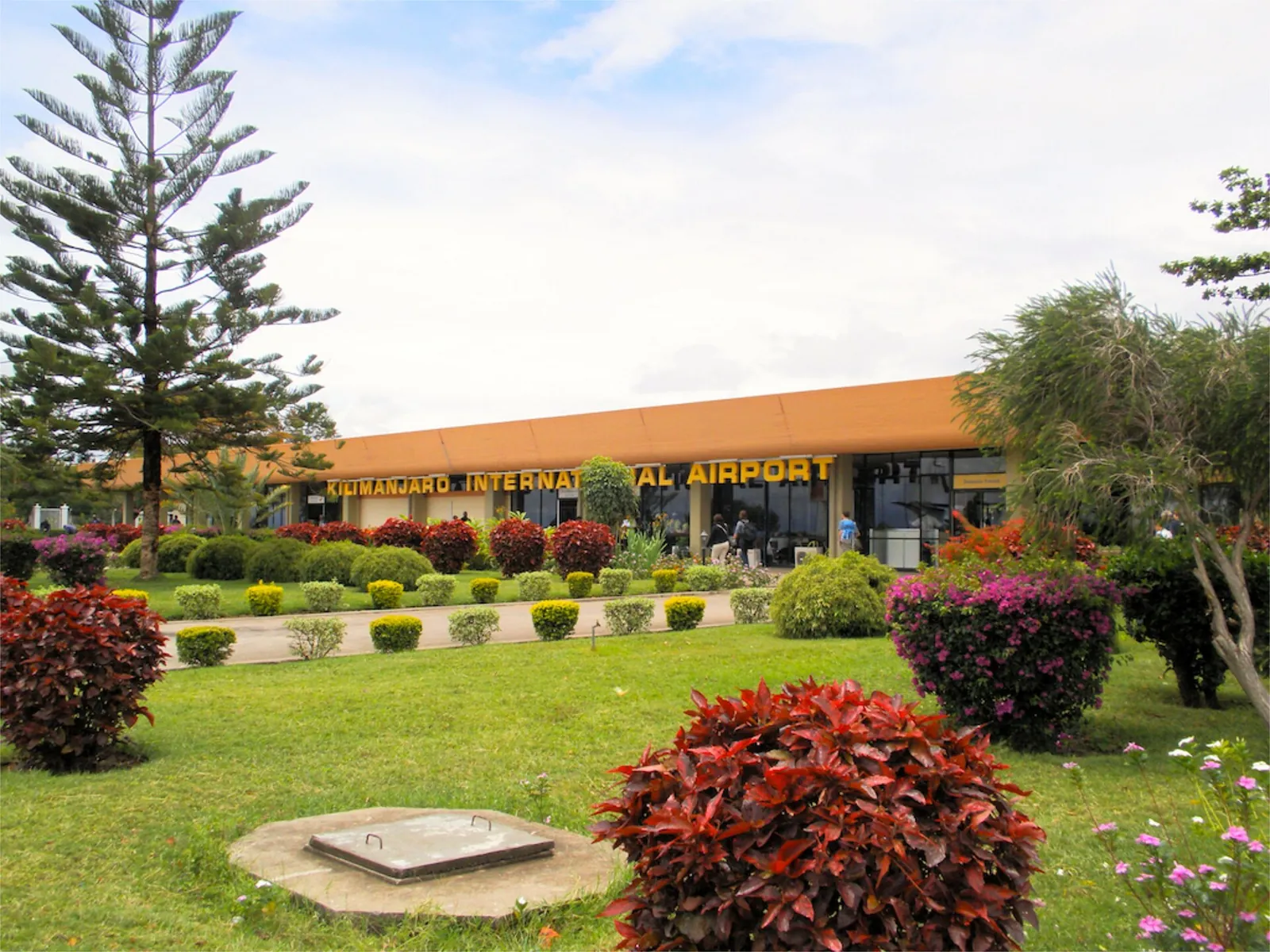 Kilimanjaro International Airport terminal with its lettering behind a garden of red shrubs and flower beds