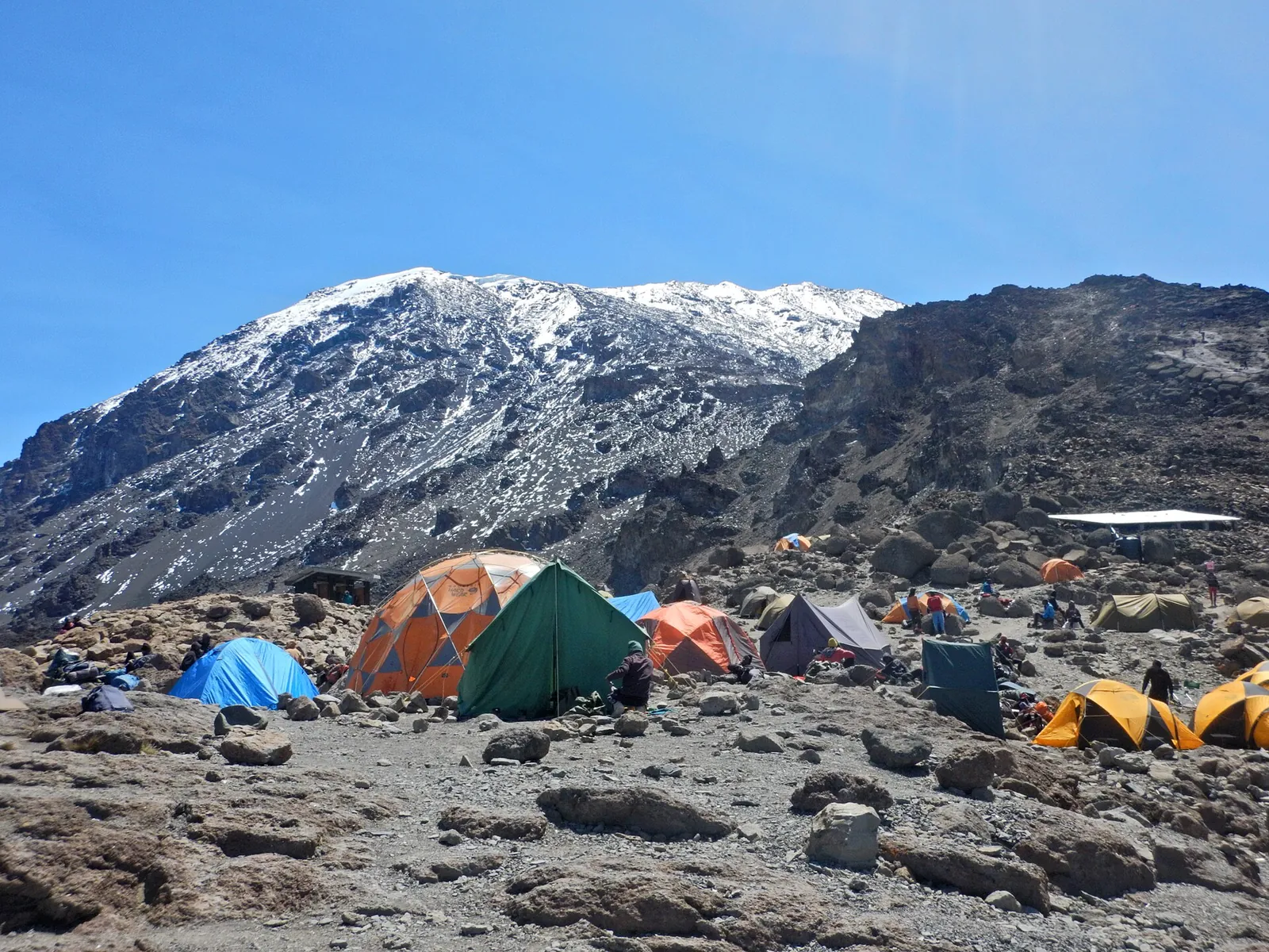 Colourful tents at Barafu Camp on stony ground in Kilimanjaro National Park, the snow-dusted summit slope of Kibo behind