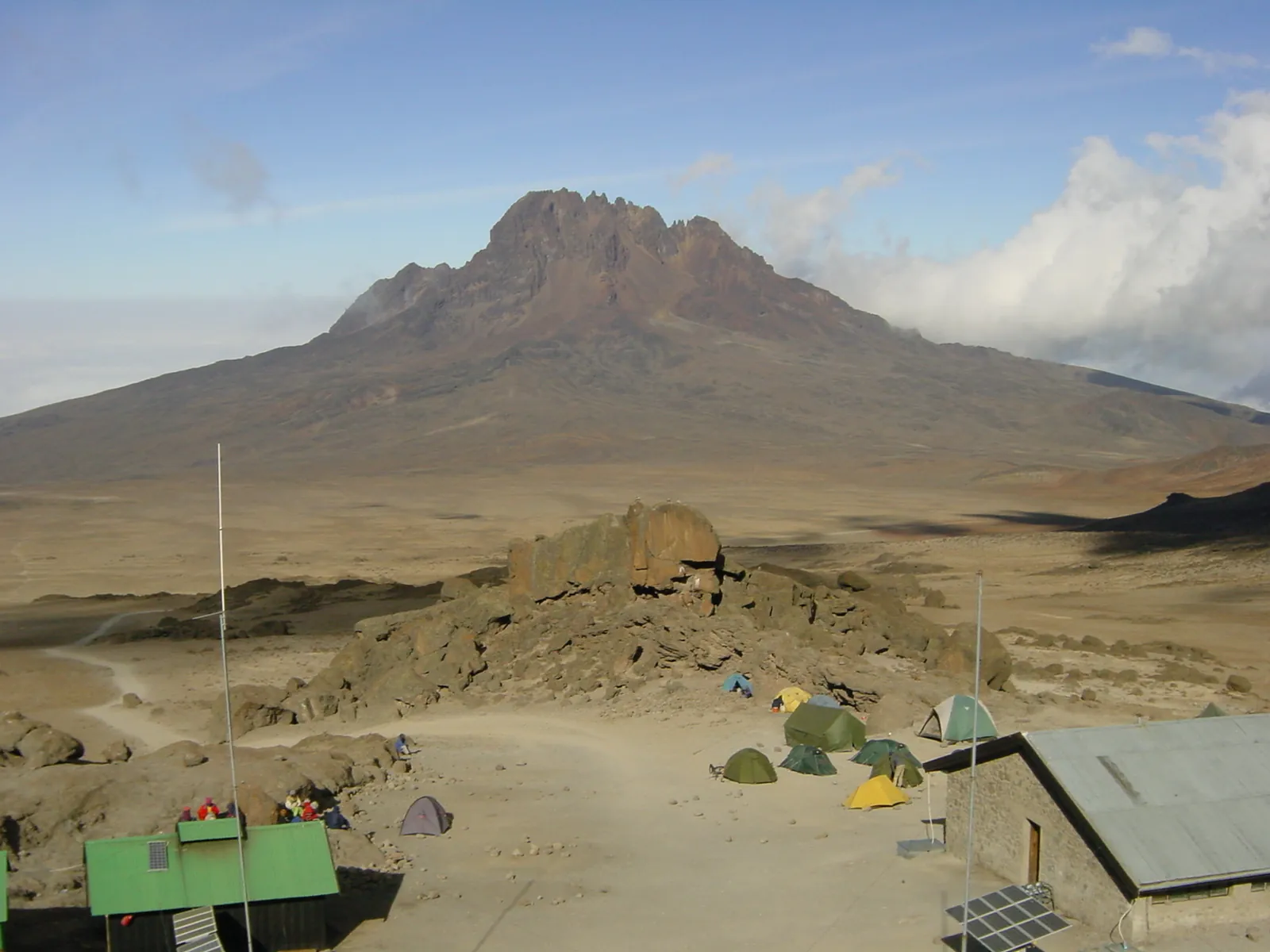 View from Kibo Huts in Kilimanjaro National Park across the alpine desert of the Saddle to the jagged Mawenzi, hut roofs and tents in front