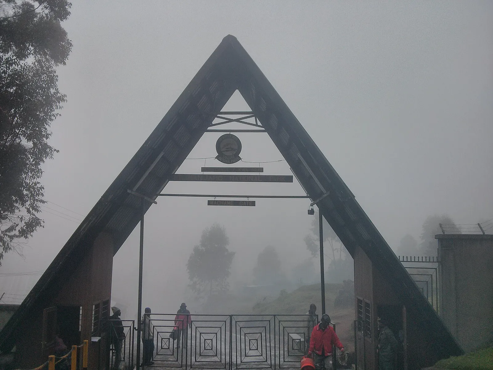 The steep A-frame gateway at Machame Gate in Kilimanjaro National Park in fog, hikers and porters beneath