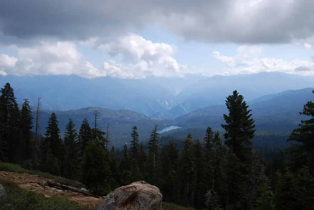 View from Panoramic Point in Kings Canyon National Park over wooded ridges and valleys, with Hume Lake far below under clouds