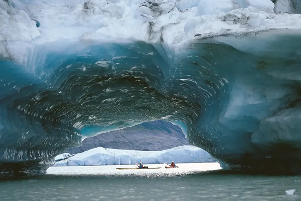 Two kayaks paddling through a tunnel in a blue iceberg on Lowell Lake on the Alsek River in Kluane National Park