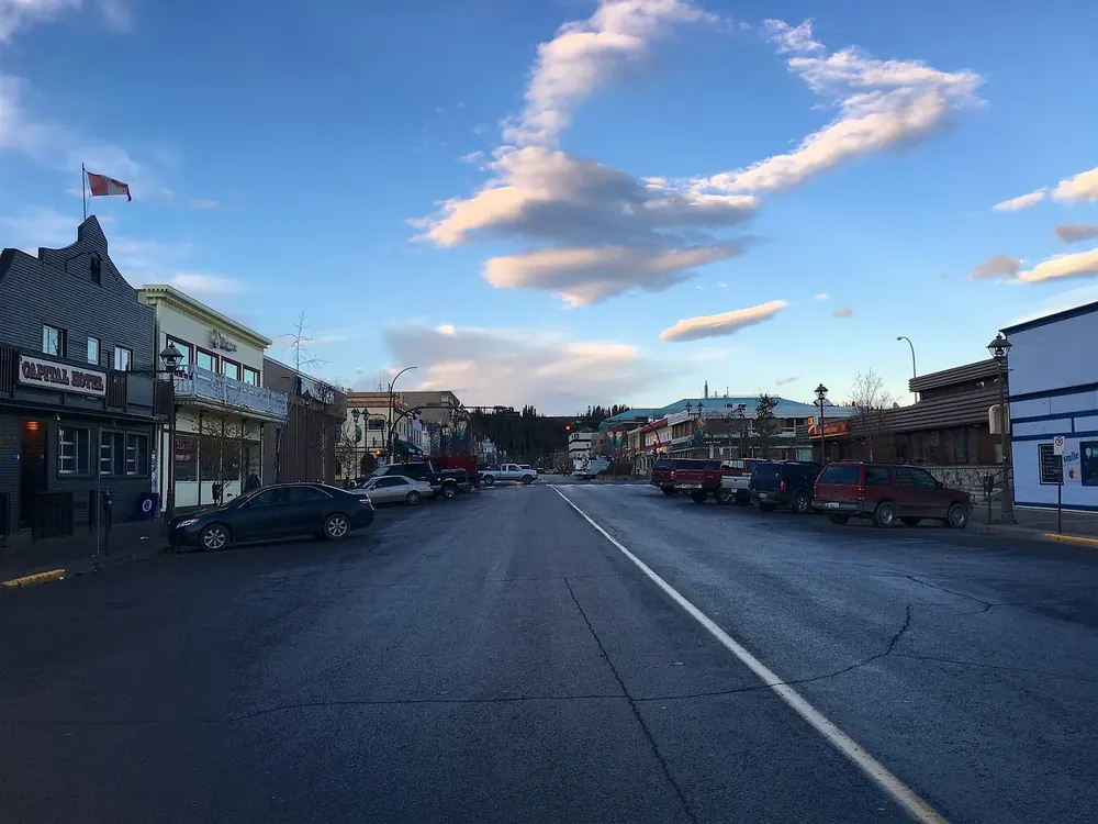 Main Street in Whitehorse in the evening sun: shops with wooden facades, parked cars and cumulus clouds