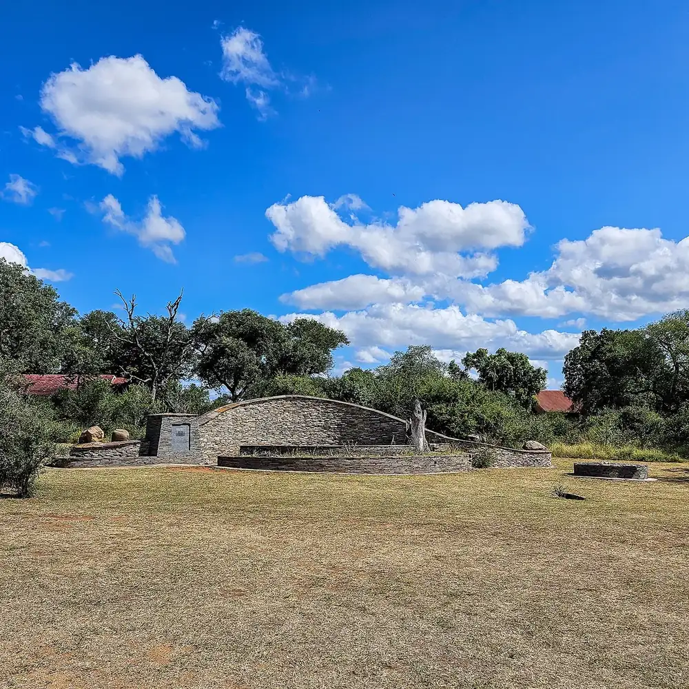 Monument at Paul Kruger Gate: a semicircular natural stone wall on a dry meadow between trees