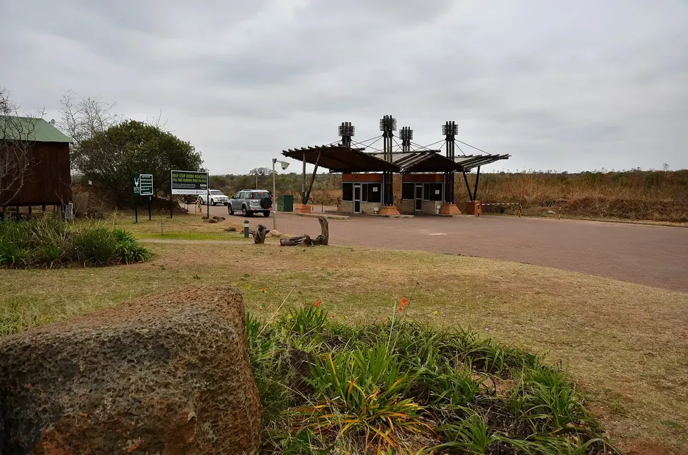 Phabeni Gate: gate building with a shady roof over the access road, rocks, lawn and bushveld in front